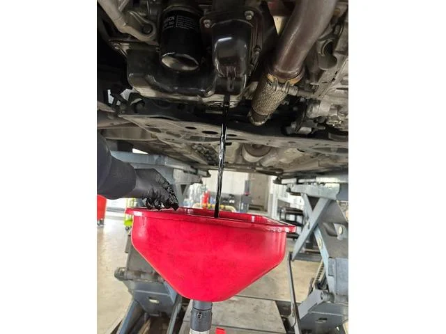 エンジンオイルを下抜きしている様子。赤いトレーに黒ずんだオイルが垂れている